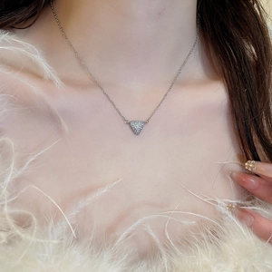 Collier triangle argenté avec zircons porté par un mannequin sur fond de plumes douces