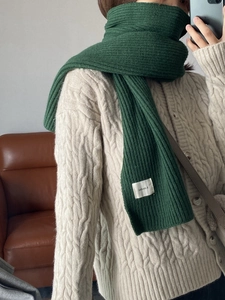 Detail shot of the green knitted scarf texture and white woven brand label