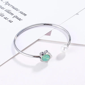 Silver open bangle featuring a green crystal flower and a white round pearl accent