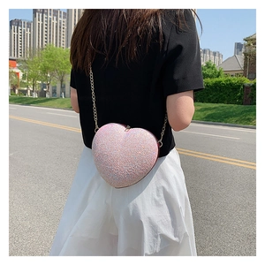 Detail of pink sequin heart-shaped crossbody bag with gold chain strap in outdoor setting