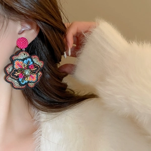 Detailed embroidered floral earring with vibrant petals and central gemstone on model