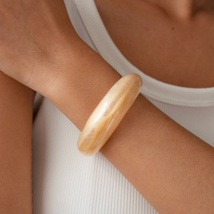 Macro detail of creamy beige resin bangle featuring marble textures on a model wrist