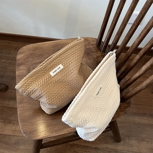 Herringbone quilted fabric cosmetic pouches in tan and cream on a wooden chair