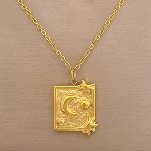 Close-up of gold titanium necklace with engraved moon and stars on a rectangular pendant