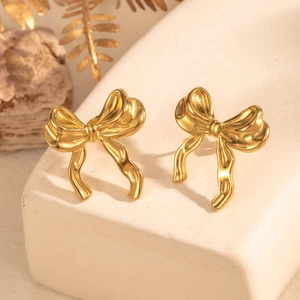 Golden bow earrings made of titanium steel displayed on a white stone pedestal