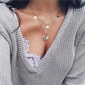 Detail of layered gold map necklace on model with world map pendant and coin charms