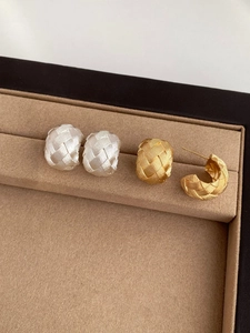 Close-up of woven texture C-shape hoop earrings in gold and silver on a jewelry tray