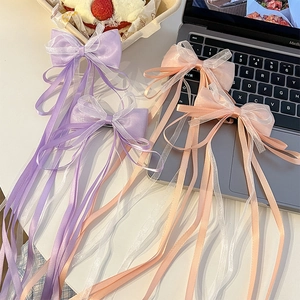 Detail view of four long ribbon bow hair clips in purple and peach colors for girls