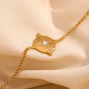 Macro view of gold-plated stainless steel bracelet featuring an etched starburst pendant