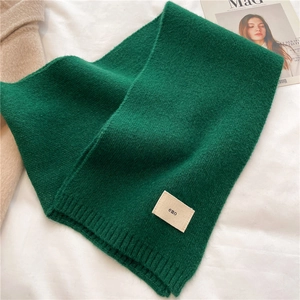 Detail of green knitted scarf texture with a stitched emo label on a minimalist background