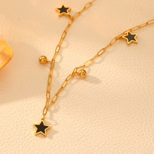 Gold chain necklace featuring black star pendants and golden beads on a textured surface