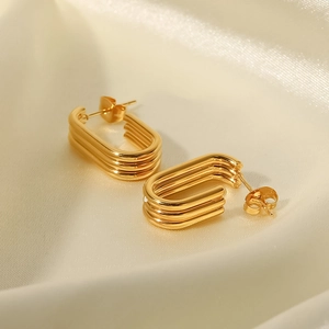 Détail de boucles d'oreilles géométriques en U à trois couches dorées sur de la soie