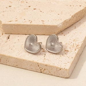 Macro shot of silver heart studs with textured finish on beige stone backdrop