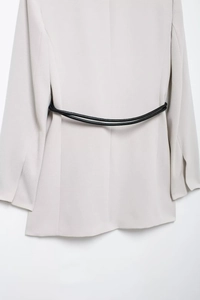 Detail view of the back of a beige blazer with two stylish black waist belts