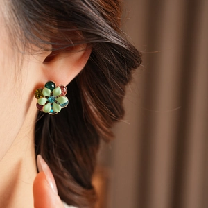 Close-up of vintage flower earrings with green petals and colorful gems worn by a model