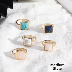 Detail of square natural stone rings with gold alloy frames on white textured fabric