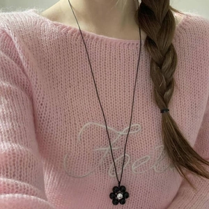 Elegant beaded necklace with black flower pendant and white bead on a pink sweater