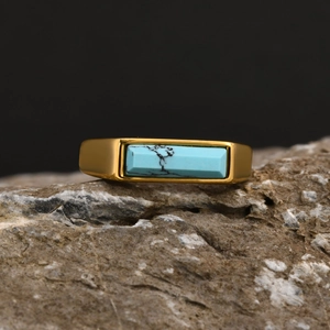 Macro view of a rectangular turquoise stone set in a gold hip hop ring on raw stone