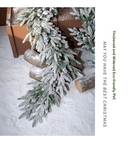 Close-up of thick PVC green Christmas garland with artificial snow and warm LED lights