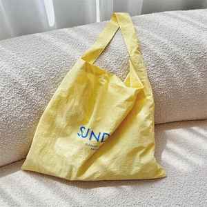 Close-up of bright yellow canvas tote bag with blue lettering on a soft cream background