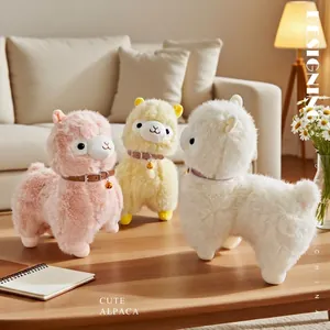 Plush alpaca dolls with bells in pink, yellow and white colors on a wooden table