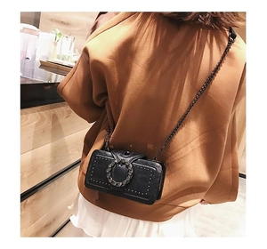 Detail of a black PU leather crossbody bag with metal chain and rivets on a model