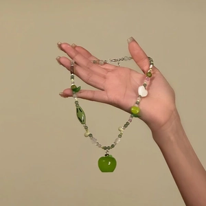 Close-up of green beaded necklace with apple pendant and white heart bead detail