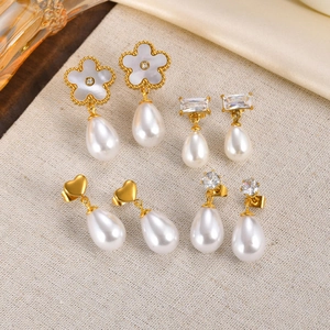 Macro shot of four pairs of gold stainless steel pearl earrings with zircon on beige fabric