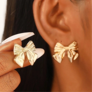 Elegant gold bow earrings with textured detail worn on ear and held by hand
