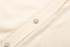 Detail eines cremefarbenen Strickcardigans mit verzierten silbernen Blumenknöpfen
