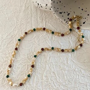 Close-up of beaded necklace with beige shell beads, green stones and freshwater pearl
