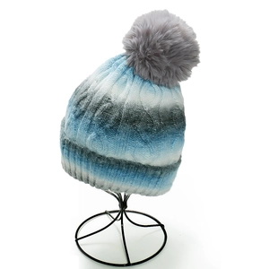 Detail of blue and white ombre winter knit beanie with thick ribbing and large fur pom-pom
