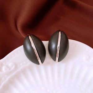 Macro shot of black oval wooden stud earring with silver stripe on ceramic plate