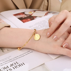 Detail of a gold coin pendant bangle on model with minimalist 18K gold plated steel design