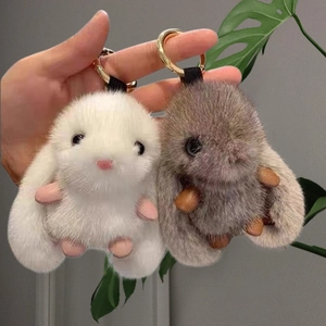 Detailed view of plush rabbit keychains in white and brown fur being held in hand