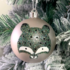 Detail of champagne silver Christmas ball with glittery fox design on a snowy tree