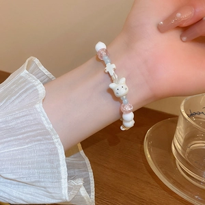 Detail of beaded bracelet featuring white cat-eye beads and cute white rabbit charm