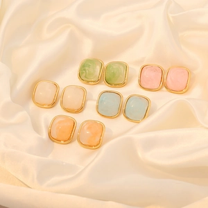 Flat lay of colorful rectangular marble resin earrings with gold edges on silk fabric