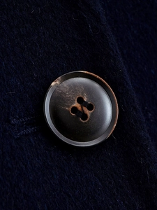 Macro shot of a vintage horn button on a dark blue wool coat with textured fabric