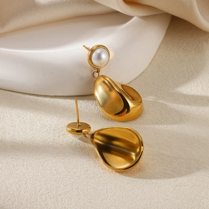 Detail view of gold water-drop earrings with white pearl studs on a minimal tray