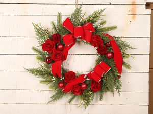 Detail of Christmas wreath with red roses, velvet bows and ornaments on white wood wall