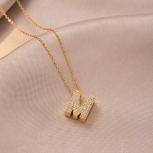Golden letter M pendant necklace with micro-set zircons on soft silk fabric background