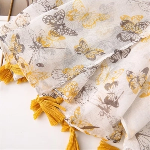 Detailed close-up of yellow tassel trim and butterfly print on light white cotton scarf