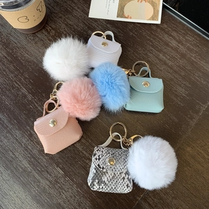 Mini leather handbag keychains with plush fur pom-poms in various colors on wood