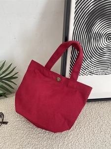 Minimalist burgundy canvas tote bag with a metal snap button and sturdy handles