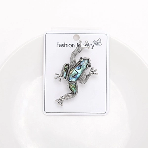 Detailed view of frog brooch with colorful abalone shell inlay on silver textured metal