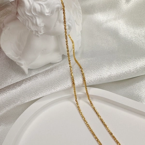 Detail of a thin gold-plated S925 silver chain draped over a white angel sculpture
