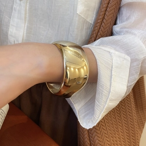 Close-up of a wide polished gold metal cuff bracelet worn on a wrist in a stylish setting