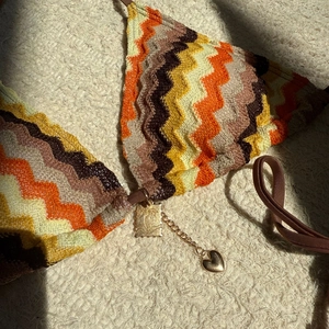 Detail of zigzag knit bikini top with golden palm tree and heart chain charms