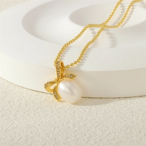 Detail of white pearl pendant with golden diamond-studded bow on a beaded chain